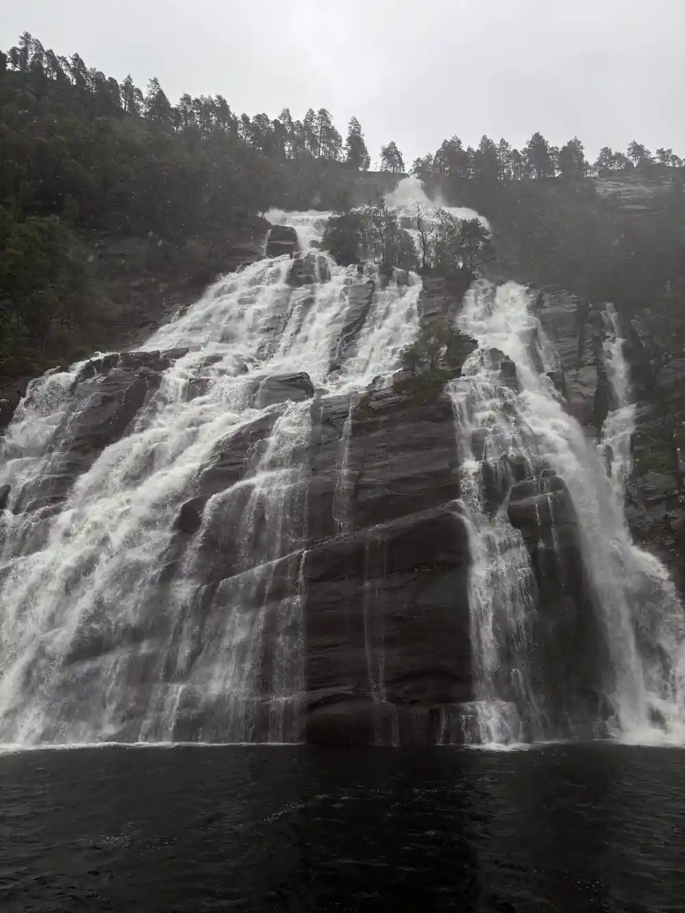 A broad waterfall over a dark cliff seen from the water
