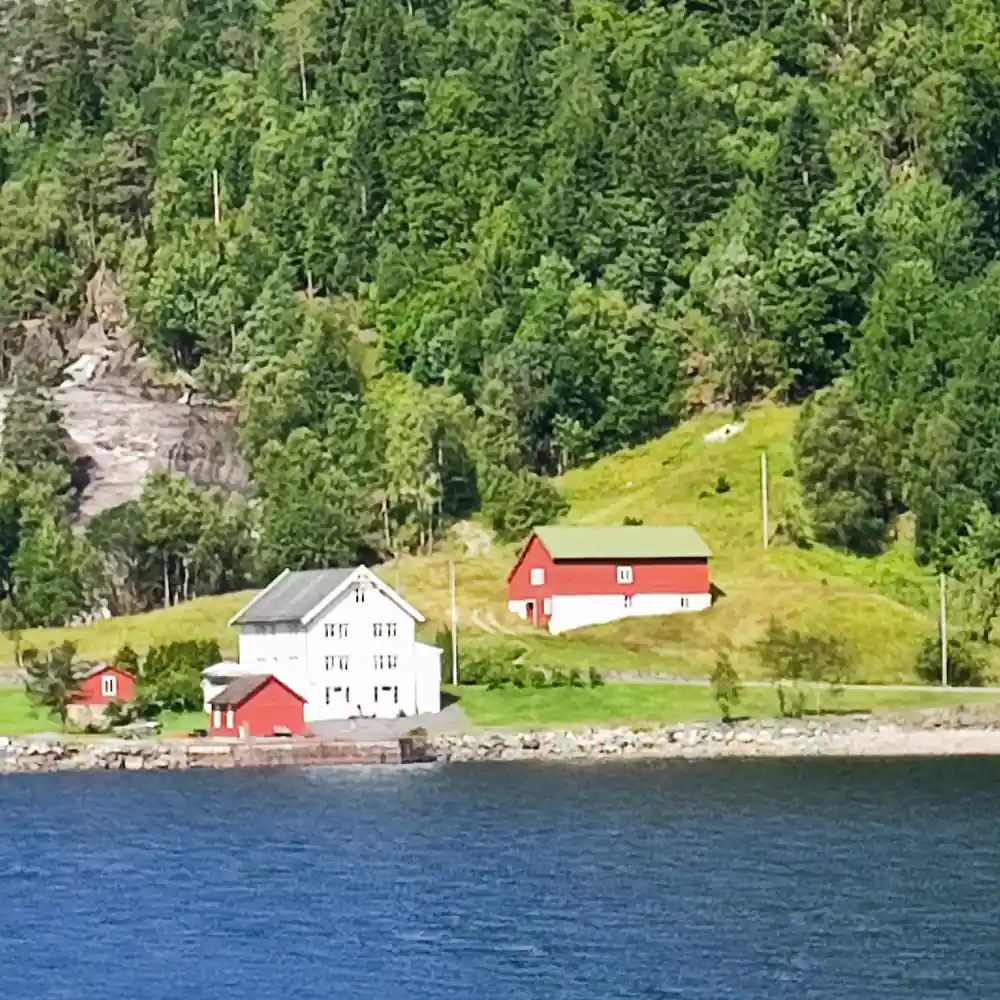 A red barn and white farmhouse on the fjord shore