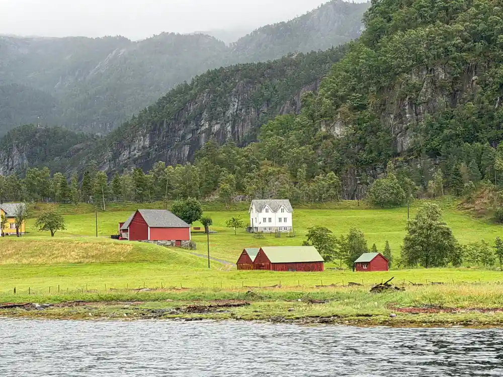 A red barn and white house on a green shoreline