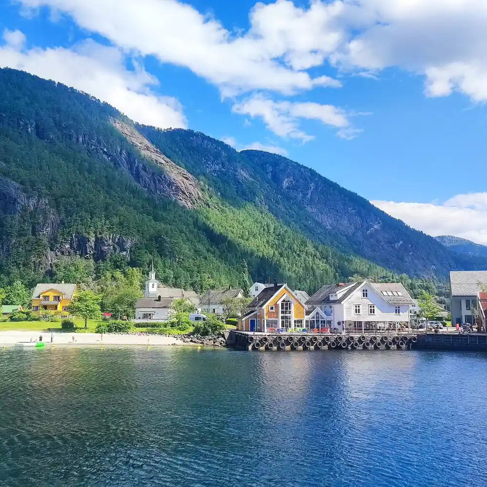 A shoreline village of painted houses below a green mountain