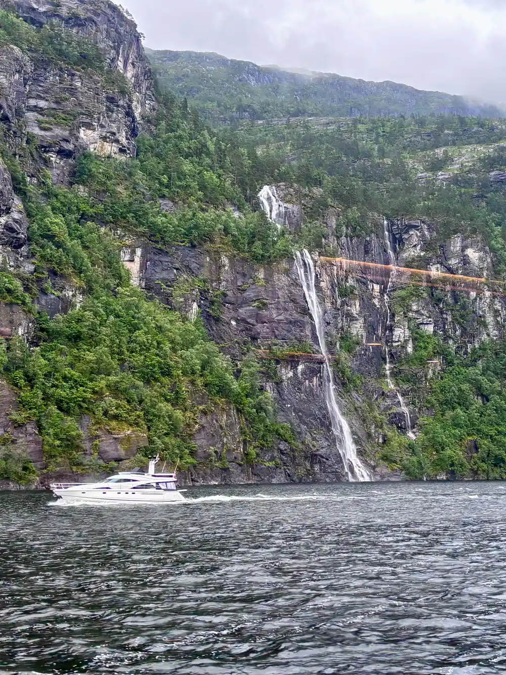 A small boat below a cliff with a waterfall behind it