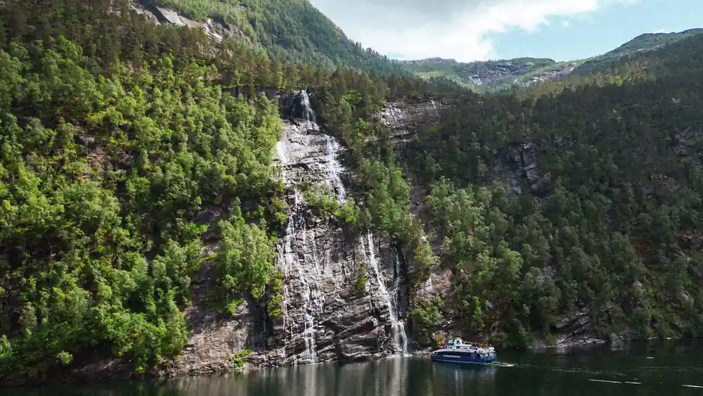 A tall waterfall falling down a wooded cliff to the water