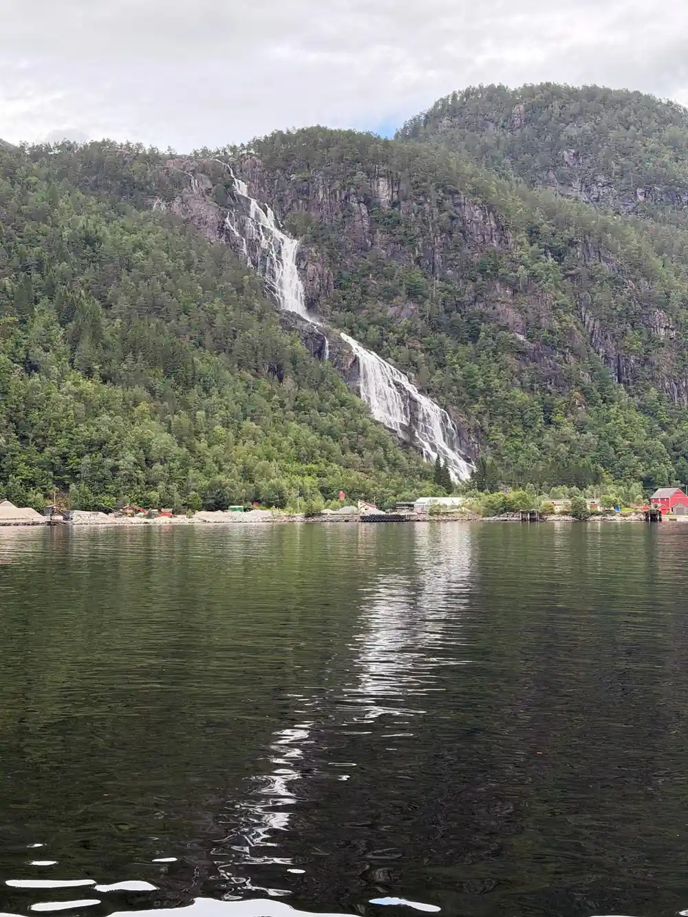 A tall waterfall on a wooded slope above the fjord