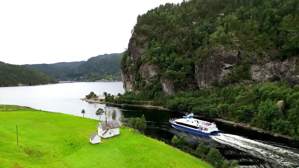 A white chapel on a green point with the vessel passing behind