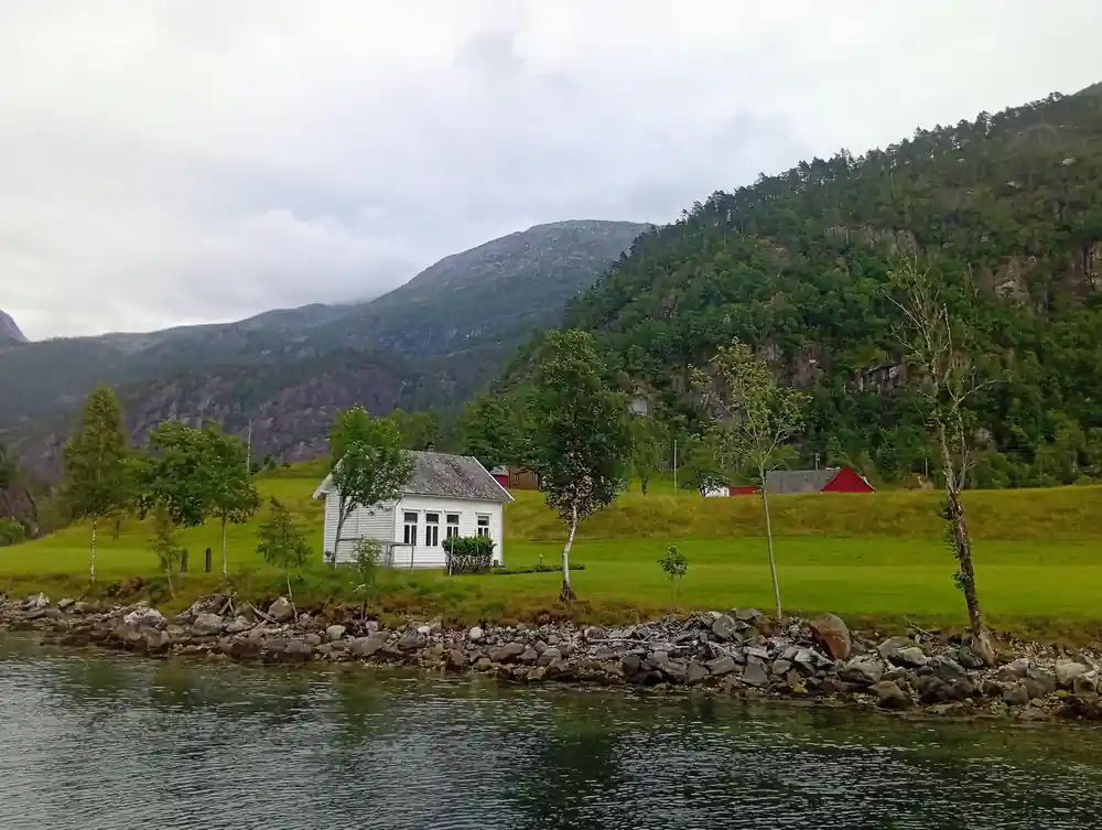A white farmhouse on a green shoreline meadow