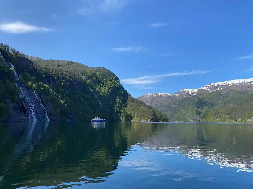 A wide calm fjord reach under blue sky with snow on the tops